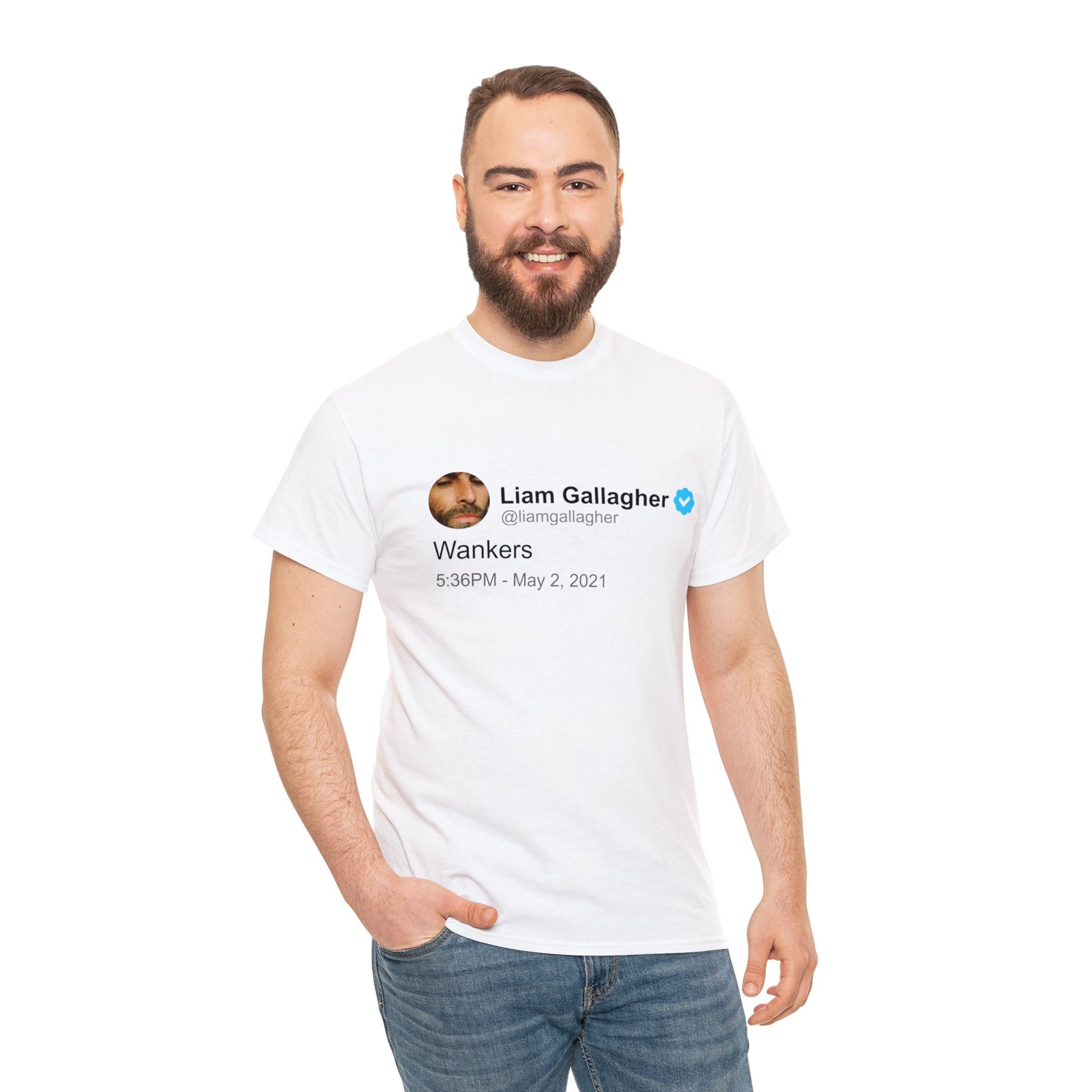 A smiling man models a white T-shirt adorned with a humorous tweet from Liam Gallagher in black text. The shirt highlights Liam's distinctive wit, offering a blend of rock 'n' roll attitude and playful humor.